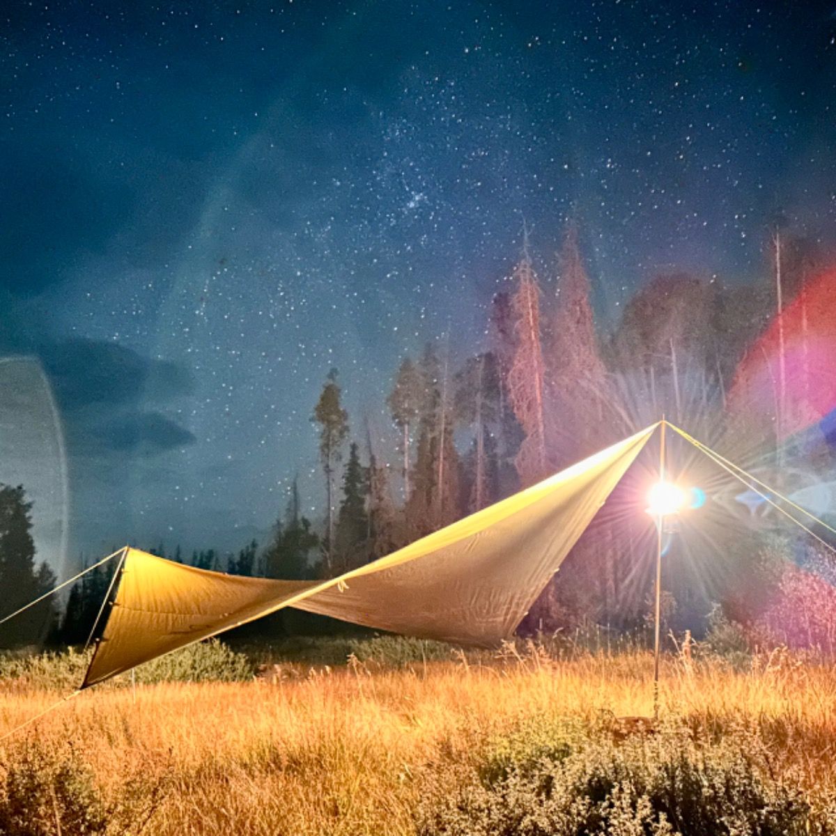 Yellow tarp set up in a field under a starry night sky with colorful lights.