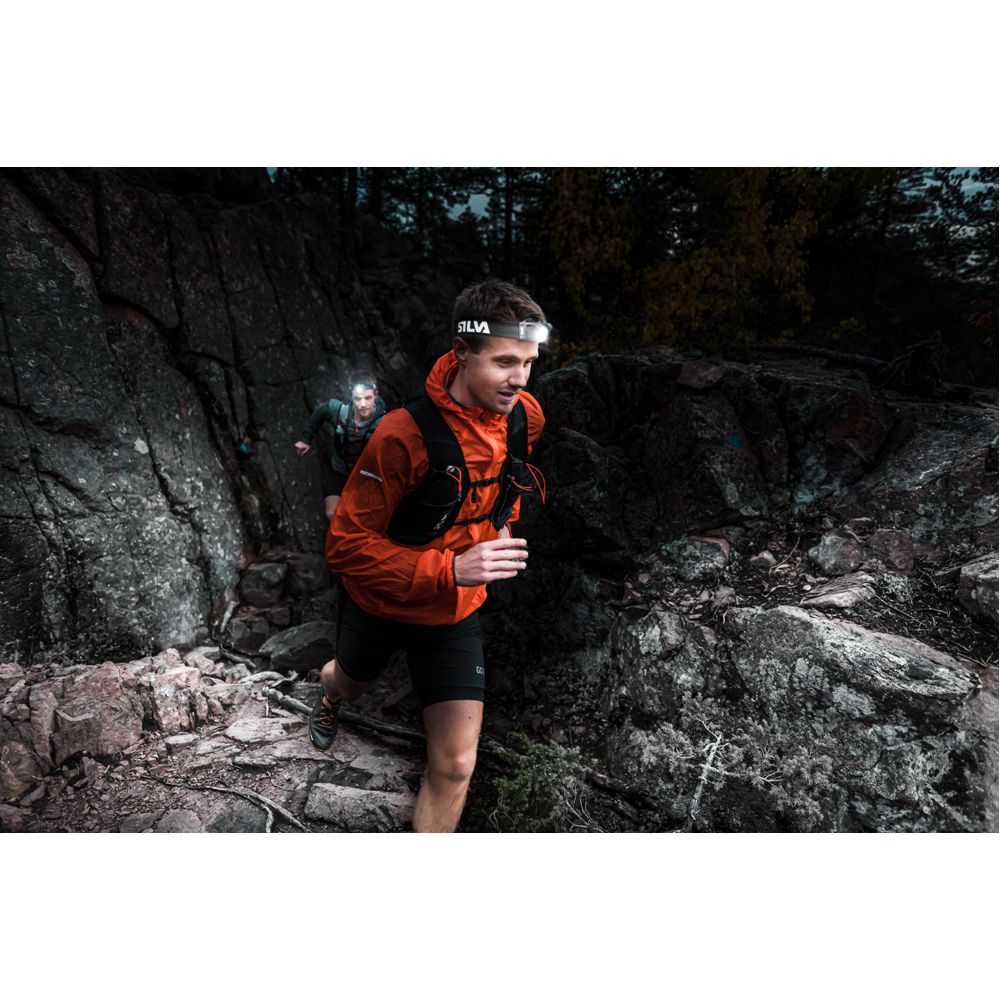 Person running on a rocky trail with headlamps in a forest setting