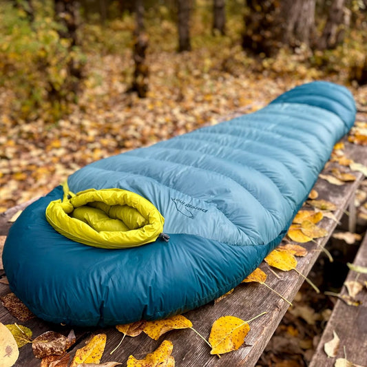Blue sleeping bag with yellow interior on a wooden bench in an autumn forest.